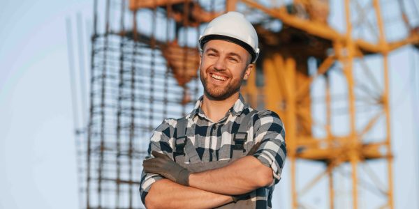Happy worker is standing on the construction site at daytime.